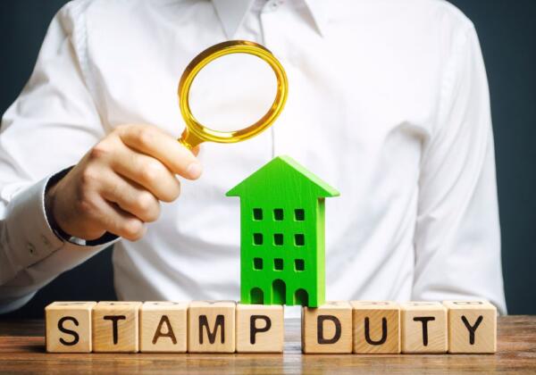 blocks spelling out stamp duty and a green house with a man holding a magnifying glass over them